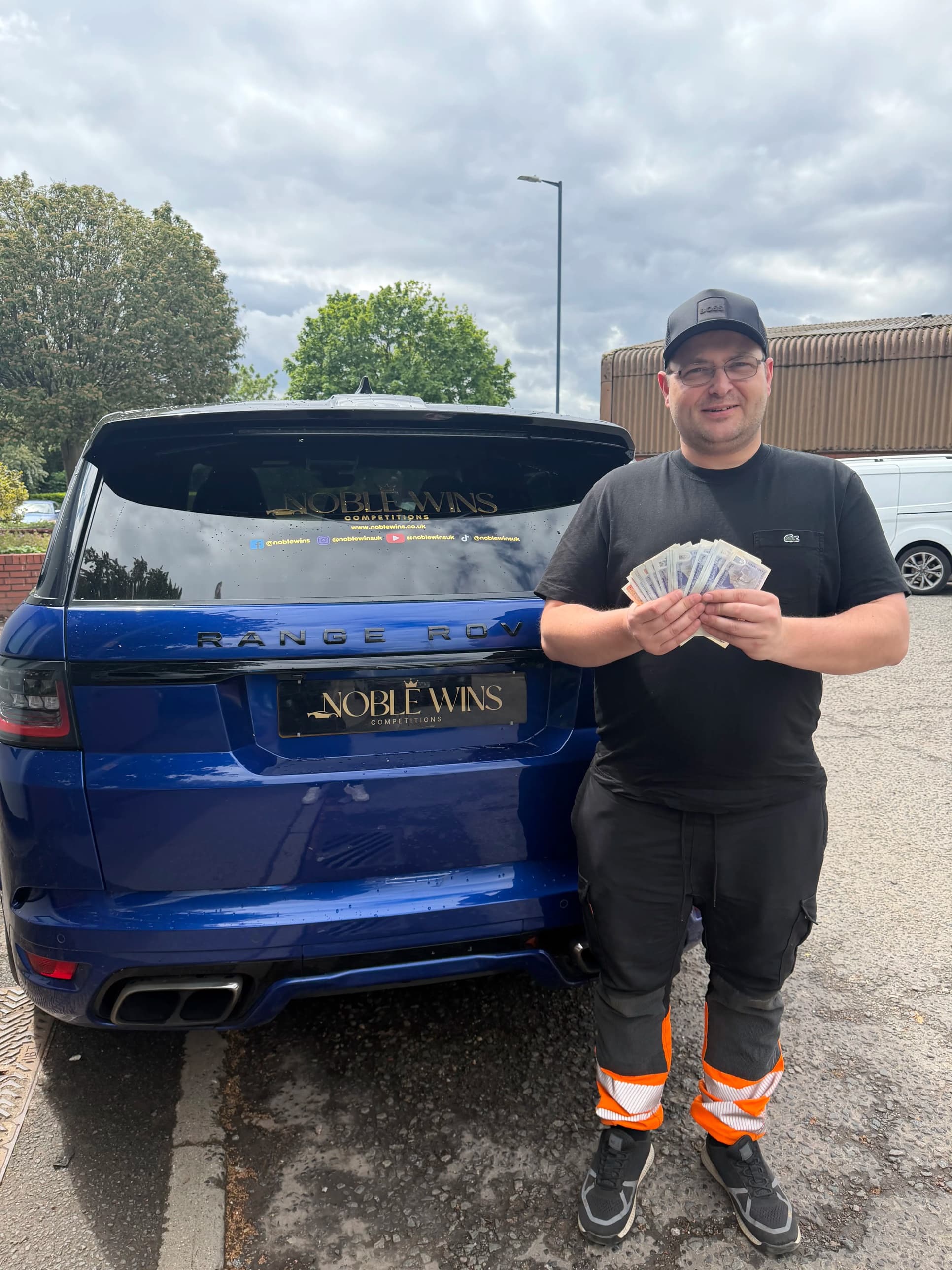 James Slevin holding £500 in cash next to a Noble Wins-branded Range Rover, after choosing the cash alternative for the PS5 + GTA V Bundle competition.